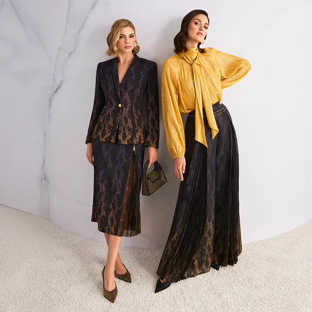 Zwei elegant gekleidete Frauenmodelle in luxuriösen Outfits mit Schlangenmuster: links ein dunkler Blazer mit passendem Midirock, rechts eine goldene Bluse mit Schleife kombiniert mit einem fließenden, dunklen Maxirock vor hellem Hintergrund.